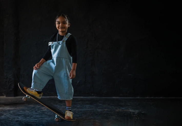 A child smiling, looking at the camera standing on a skateboard